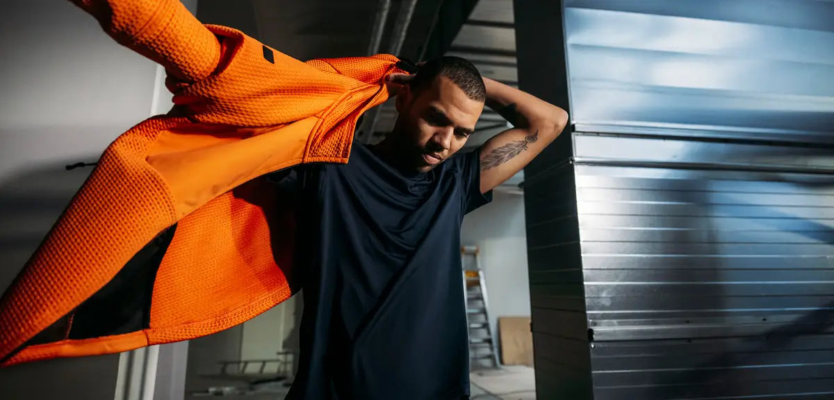 Tradesman in a Snickers Workwear T-shirt pulling on an orange jacket